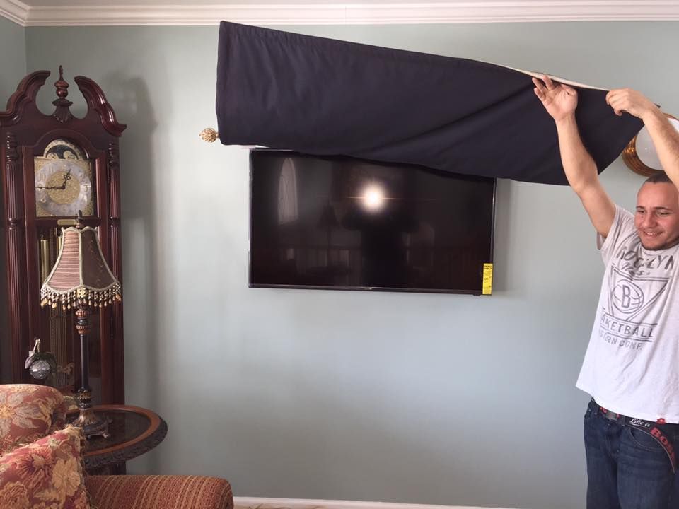 Man covering a wall-mounted TV with a dark blue cloth, in a living room with a clock and blue walls.