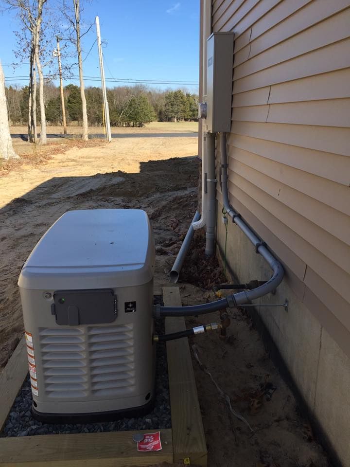 A standby generator installed next to a house. Gray generator with connected gas and electrical lines.