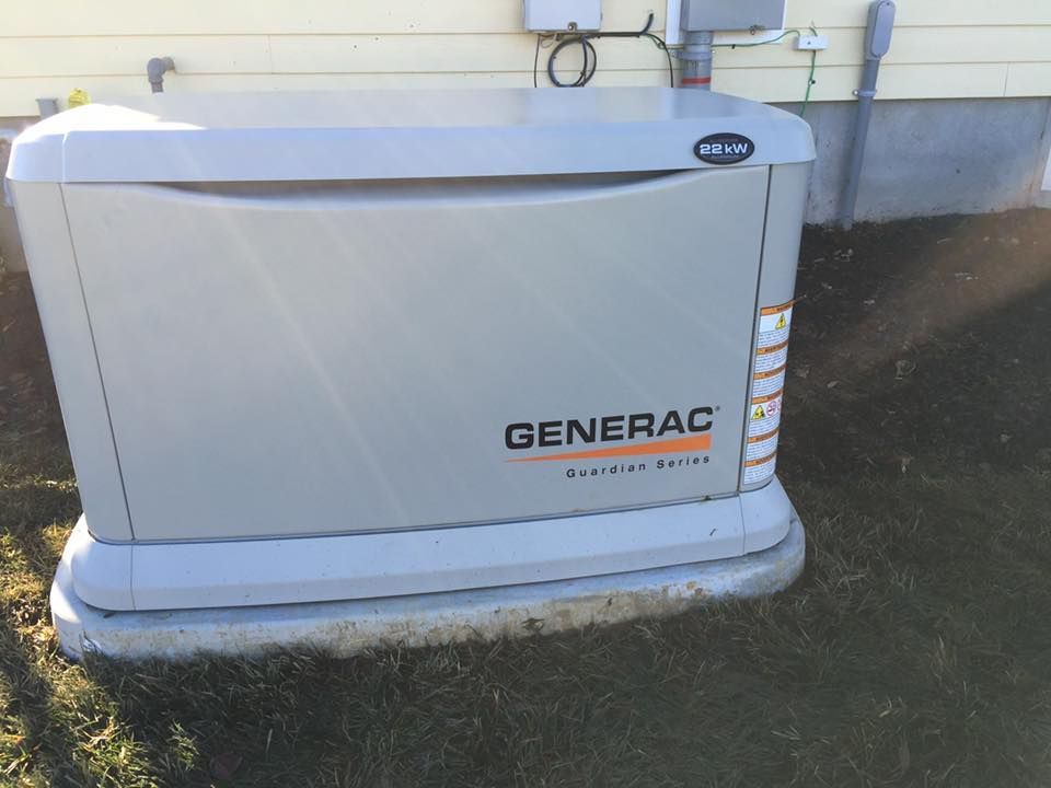 A Generac standby generator, beige and gray, installed outside a house on a concrete pad.