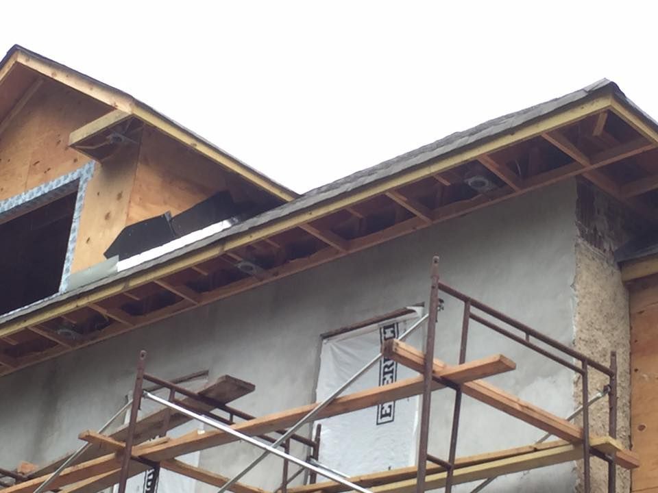 Construction of a house with scaffolding, framing, and stucco siding visible.