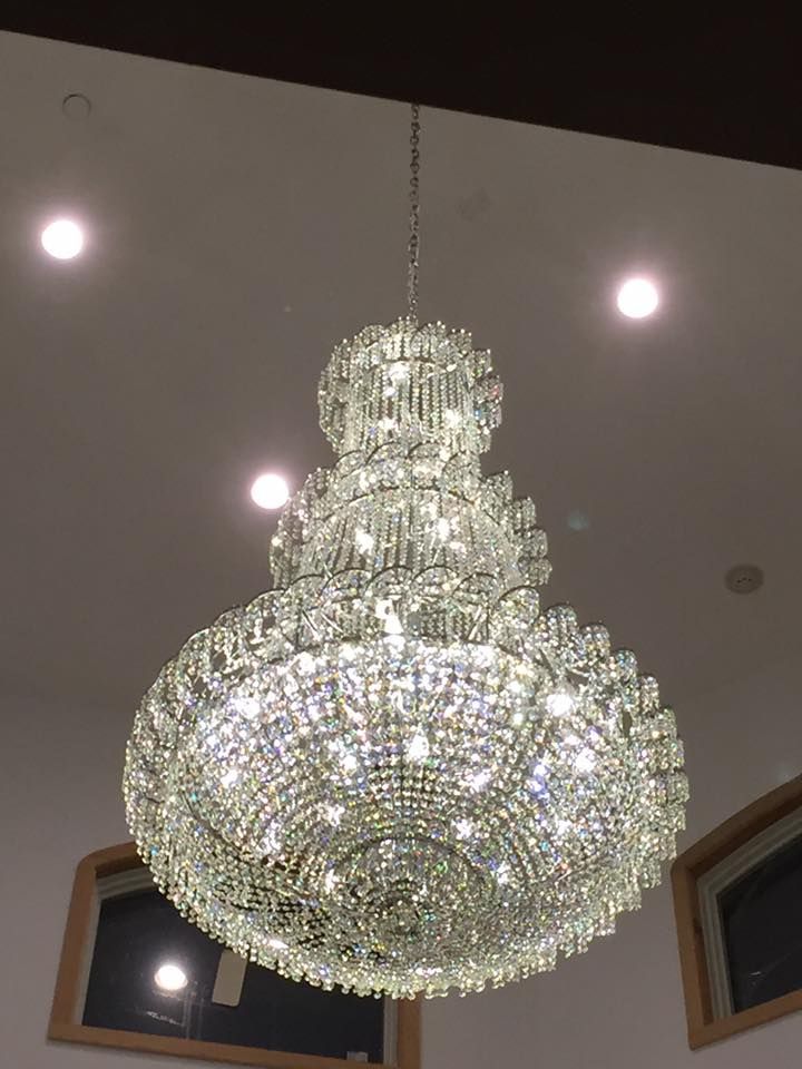 Large, ornate crystal chandelier hanging from a white ceiling, with recessed lights visible.