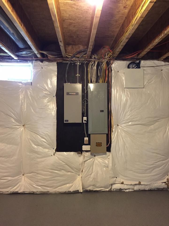 Electrical panels and boxes mounted on a black painted wall in a basement; surrounded by white insulation.