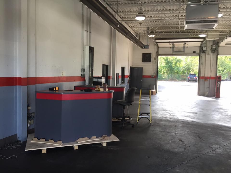A garage bay with gray and red walls, two dark gray service desks, and an open door to the outside.