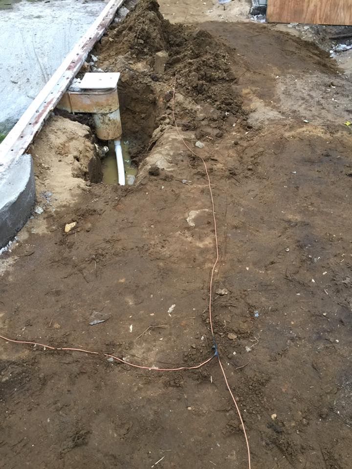 Dirt trench with electrical conduit and copper grounding wire; outdoors.
