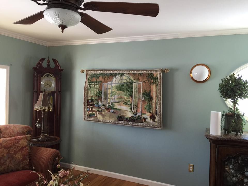 Living room with a green wall, a tapestry, grandfather clock, and a ceiling fan.