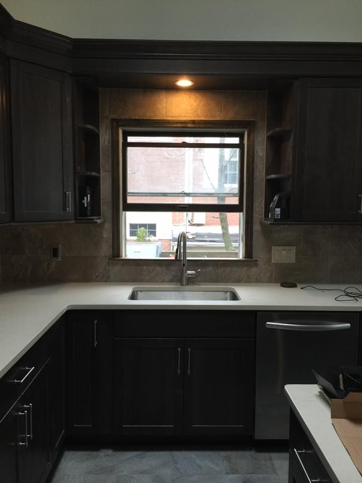 Dark brown kitchen with a window above the sink, cabinets, and a white countertop.
