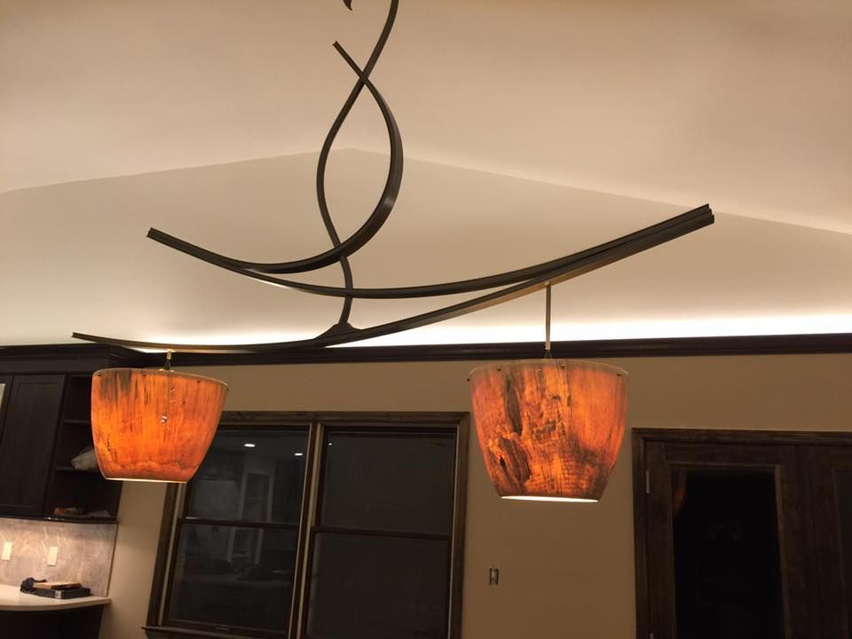 Modern light fixture with two orange lamps hanging from curved dark metal rods.