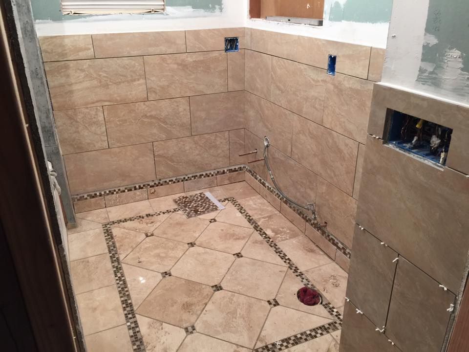 Bathroom under construction; tan tiled walls and floor with diamond pattern, small mosaic border.