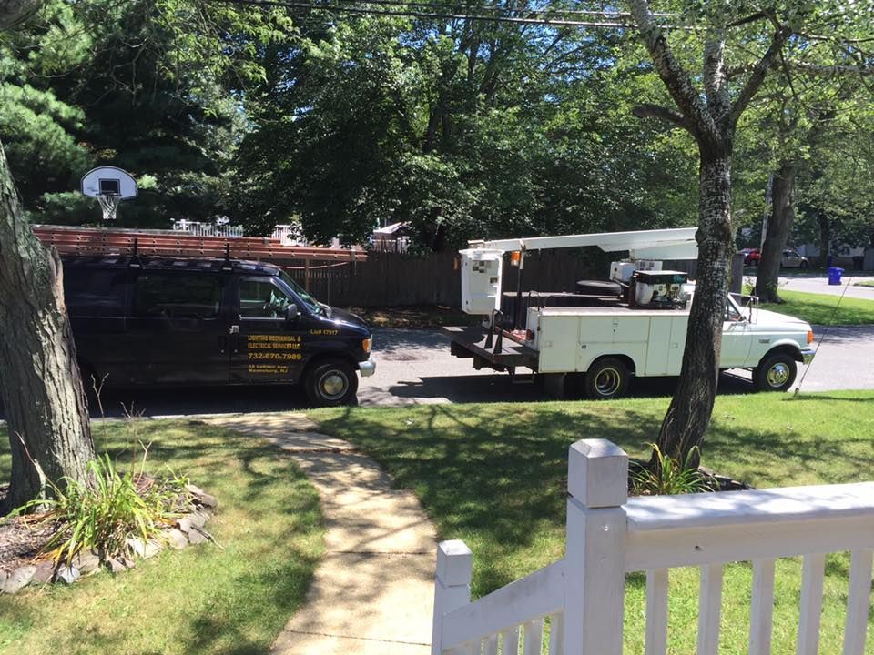 Black van and white truck with a lift parked on a residential street; trees in the background.