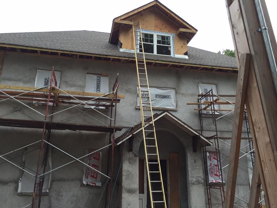 House under construction; scaffolding, ladder, and unfinished stucco exterior.