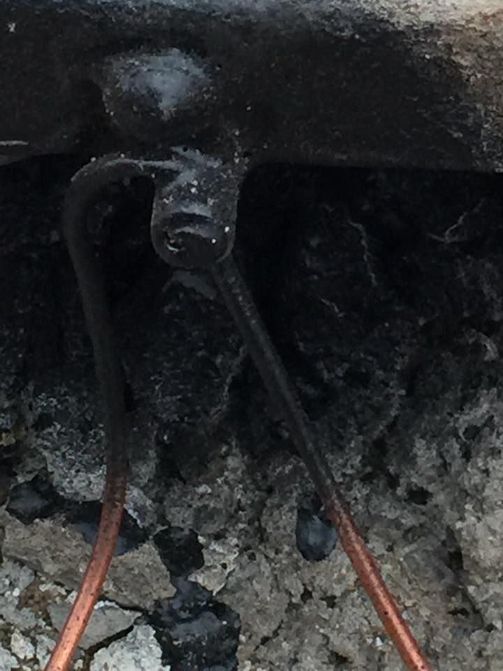 Burnt, black heating element with copper wires against a gray, ashy background.