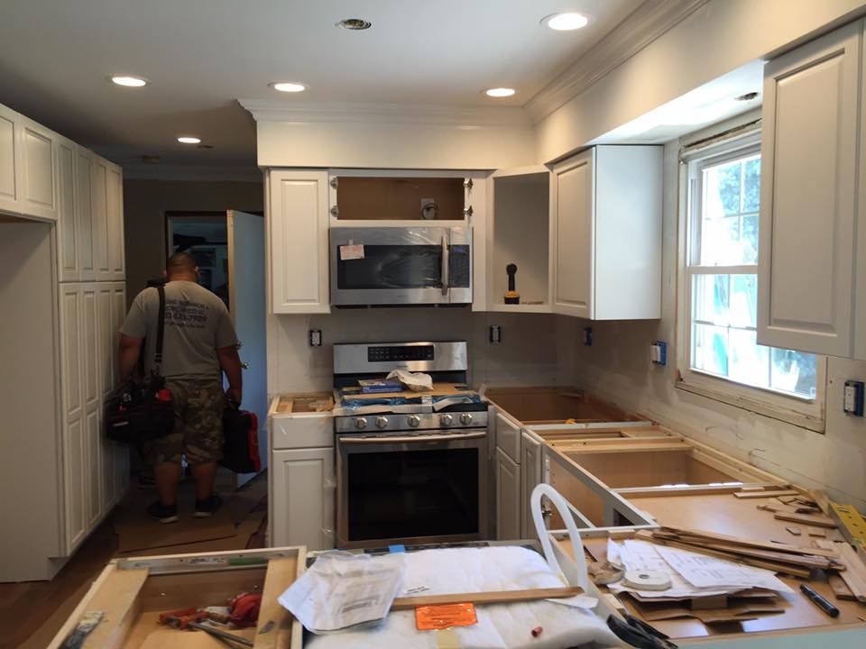 Kitchen remodel in progress: cabinets, appliances, worker in t-shirt walks toward doorway, boxes & tools.