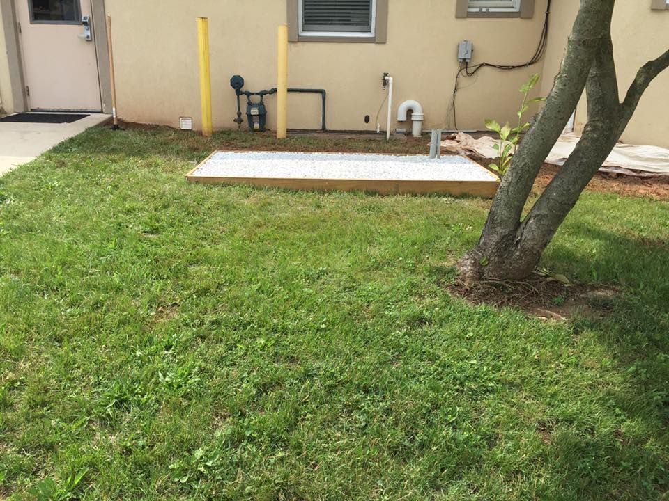 Grassy yard with a wooden-framed ground unit, gas meter, and a tree by a building's wall.