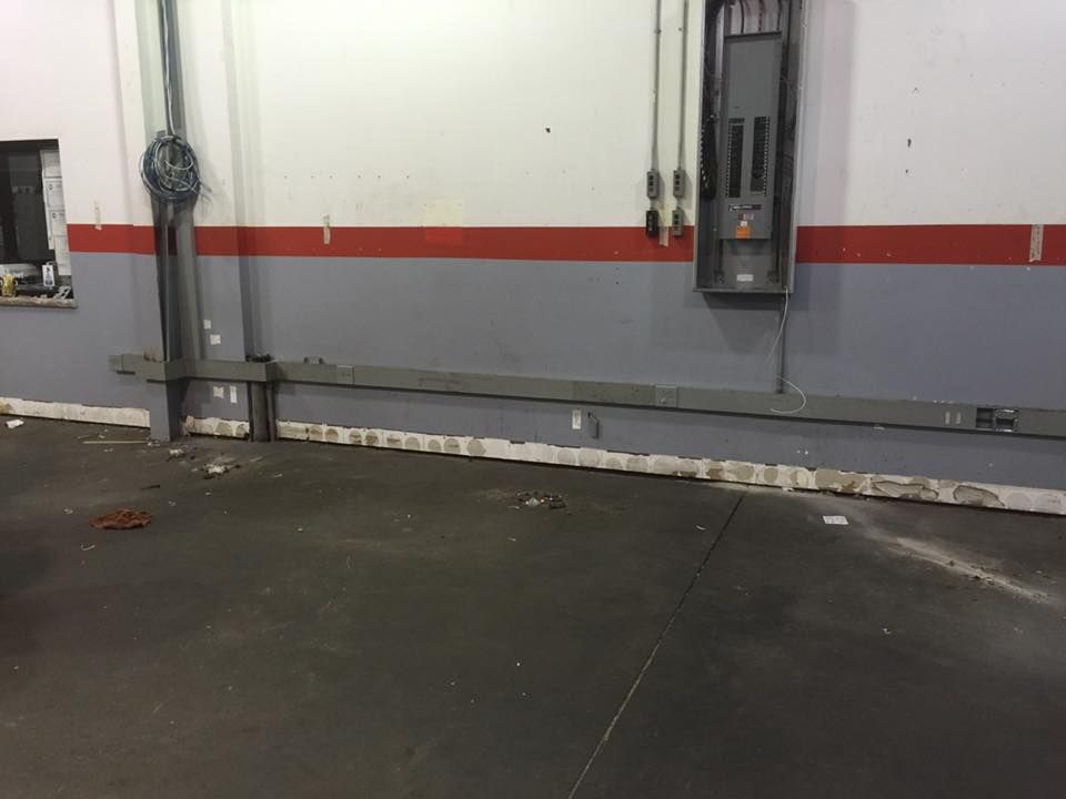 Interior of a garage with gray floor, white wall, and gray/red stripe with electrical conduit along the wall.