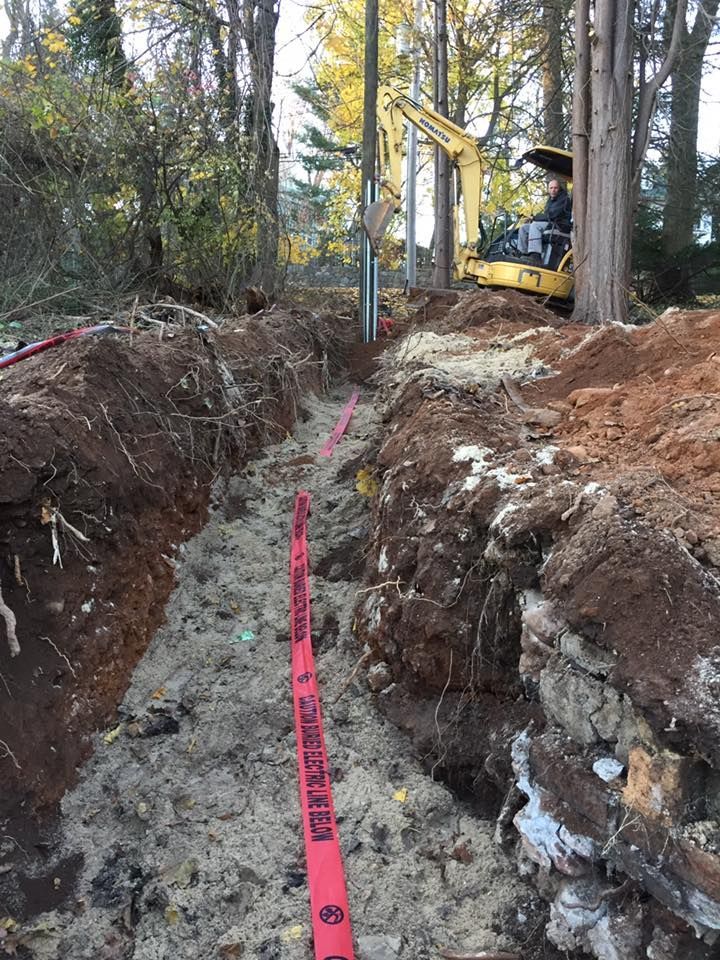 Trench dug for utilities with an excavator. Red levels mark the trench, wooded background.