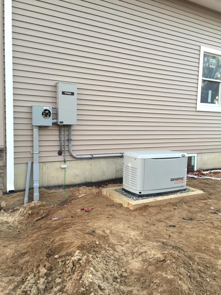 An outdoor standby generator and electrical panel installed on the side of a house with tan siding.
