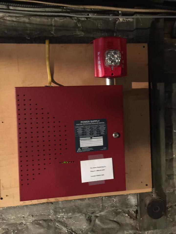 Red fire alarm panel and strobe light mounted on a wooden board in a basement.