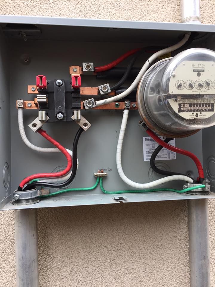Electrical meter box with wires and connections; red, black, white, and green wires against a gray metal background.