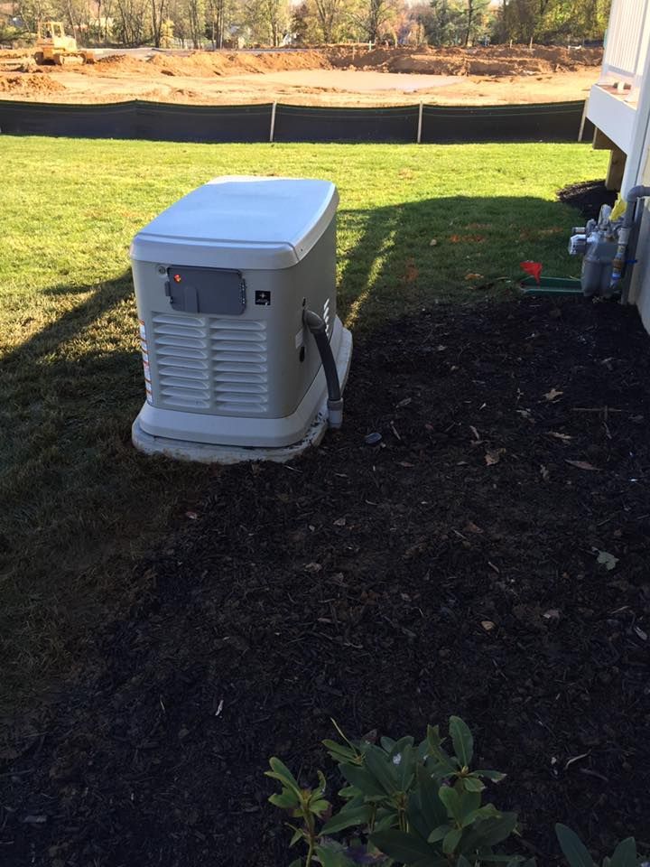 A home standby generator in a yard with mulch and grass, near a house.