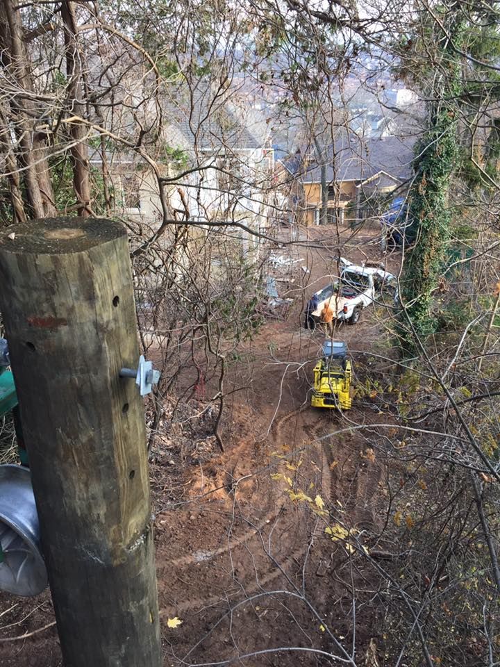 Construction site on a hillside, with a yellow bulldozer, cars, and houses visible in the background.