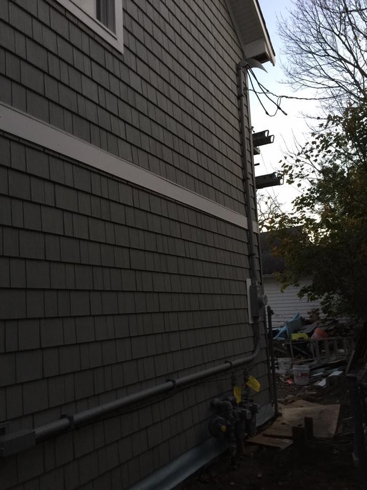 Side of a house with gray siding and electrical conduit running along the wall.