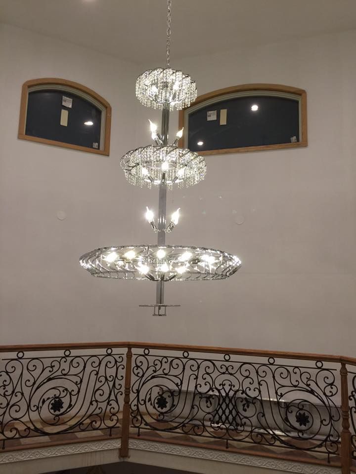 Three-tiered crystal chandelier hangs in a foyer with arched windows and ornate railing.