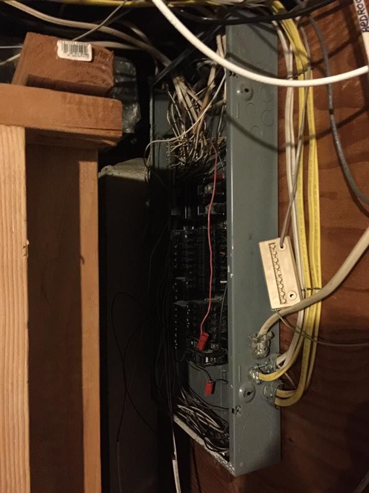 Electrical panel with exposed wires in a dimly lit wooden room.