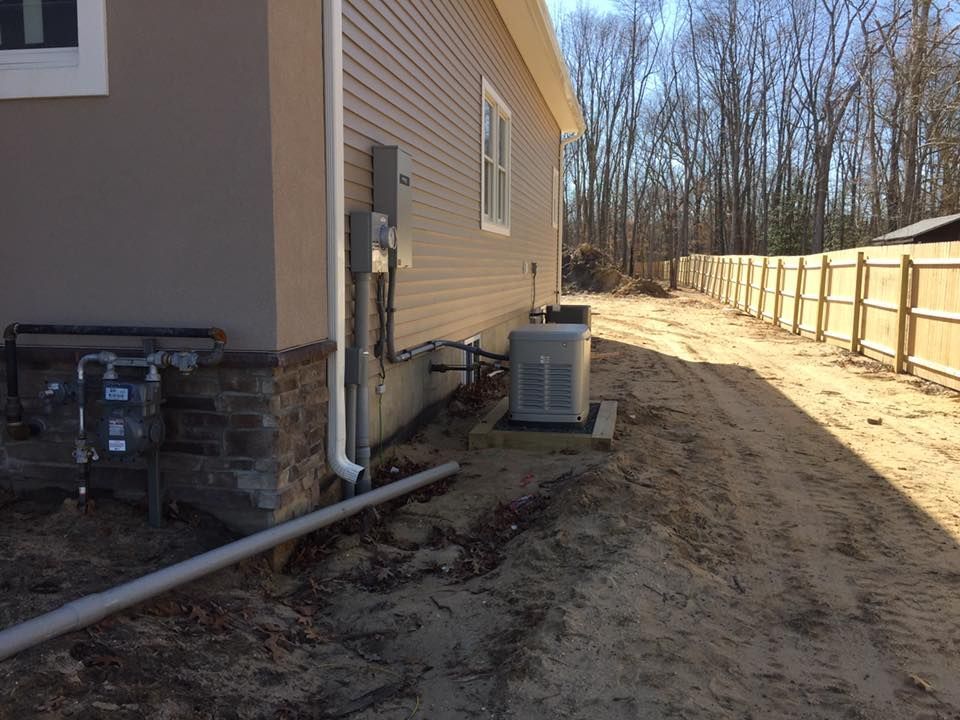 Side of house with utility meters, HVAC unit, and gravel path along a wooden fence.