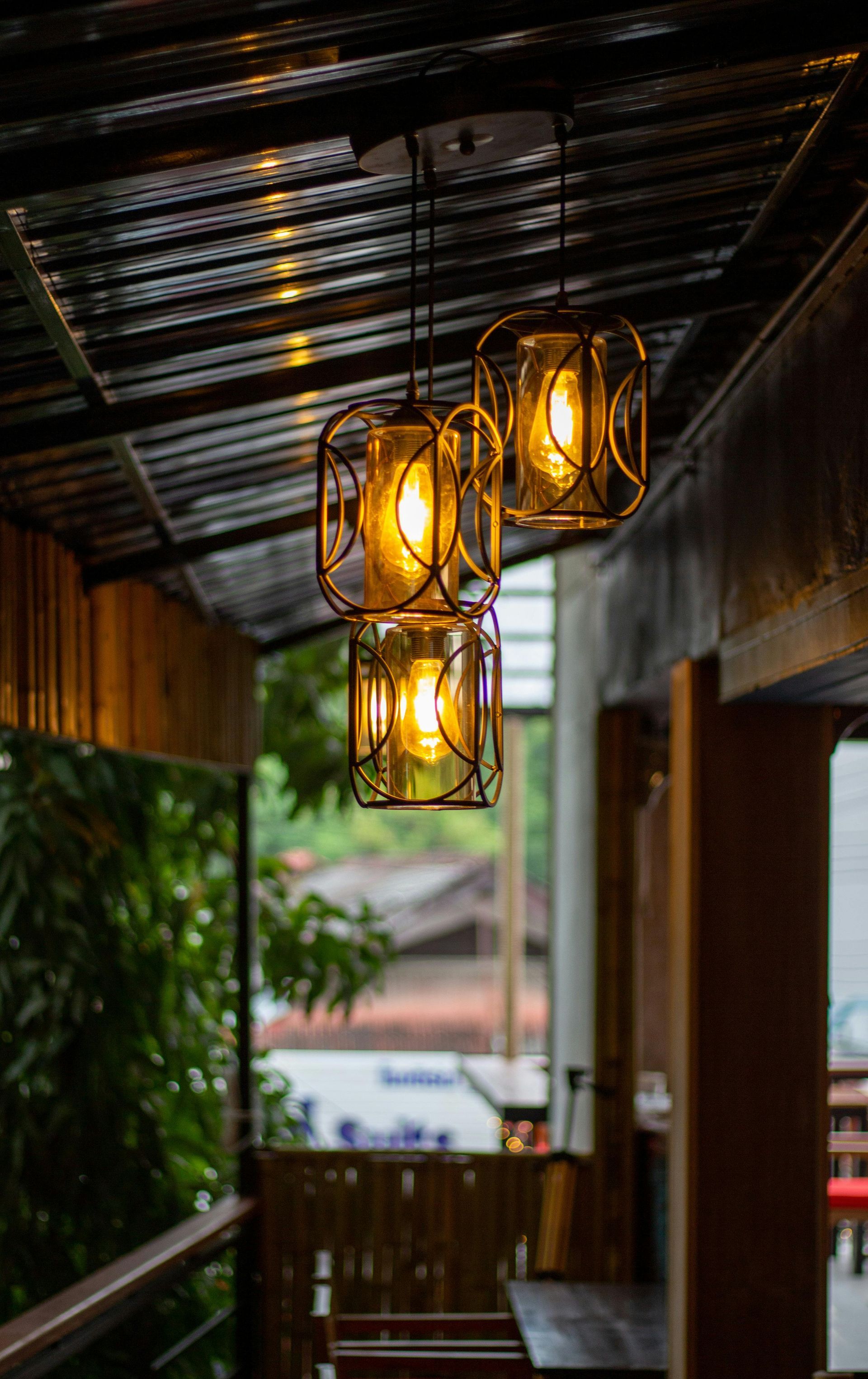 Three glowing lanterns hanging from a corrugated metal roof over an outdoor seating area.