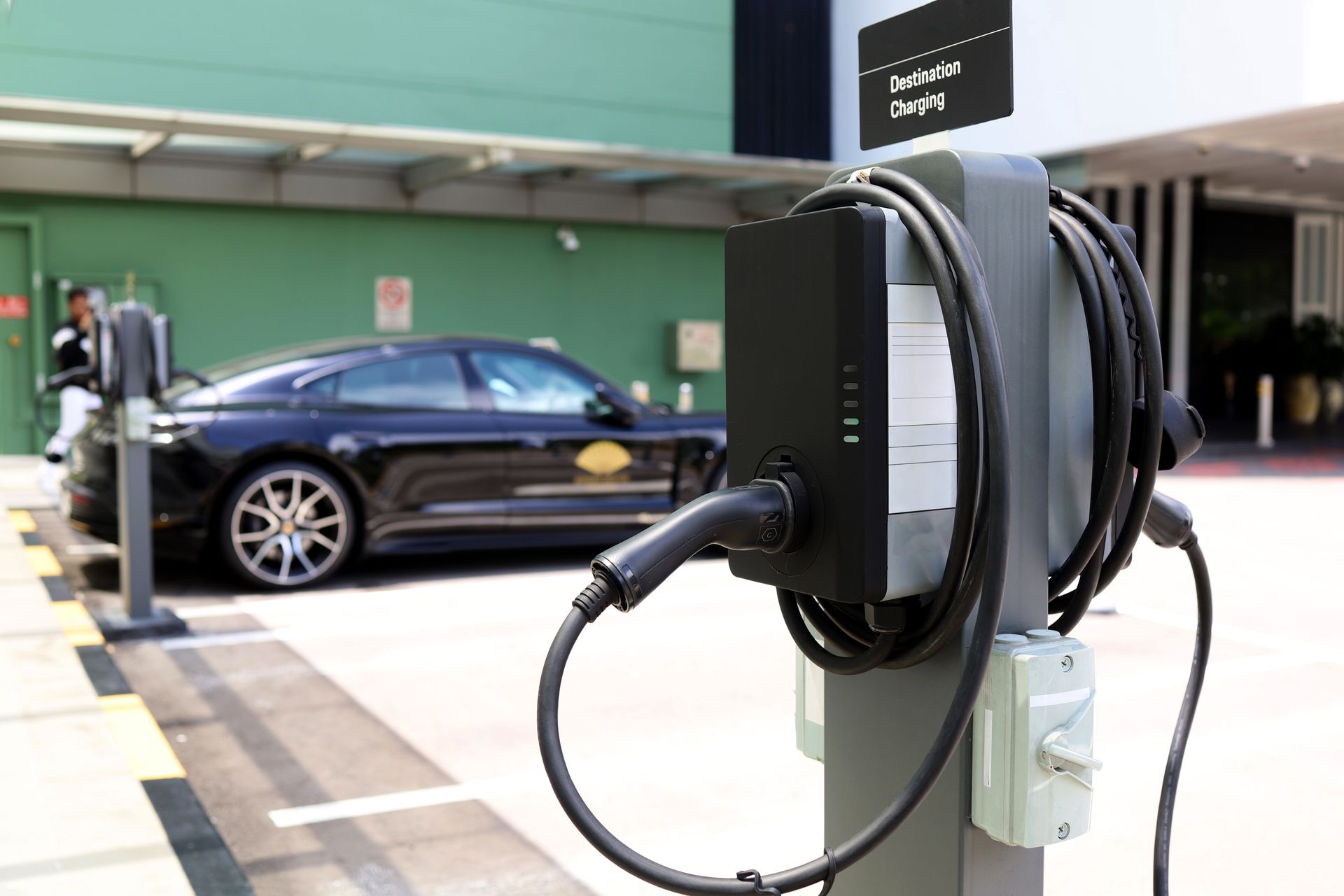 Black electric car charging at a station outside a building; sign reads 