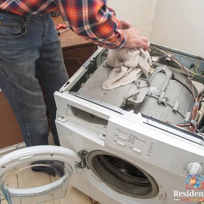 A man in a plaid shirt is working on a washing machine.