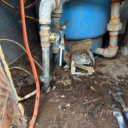 A water pump is sitting in the dirt next to a blue tank.