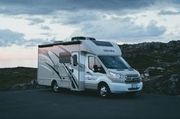 RV parked on asphalt near a rocky landscape under a cloudy sky.