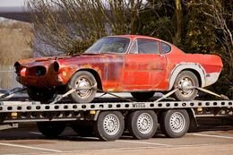 Rusty red Volvo P1800 on a car trailer, likely being transported.