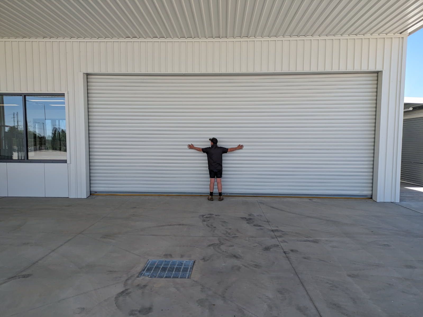 A man is standing in front of a garage door with his arms outstretched  — Goldfields Garage Doors & Gates in Wendouree, VIC