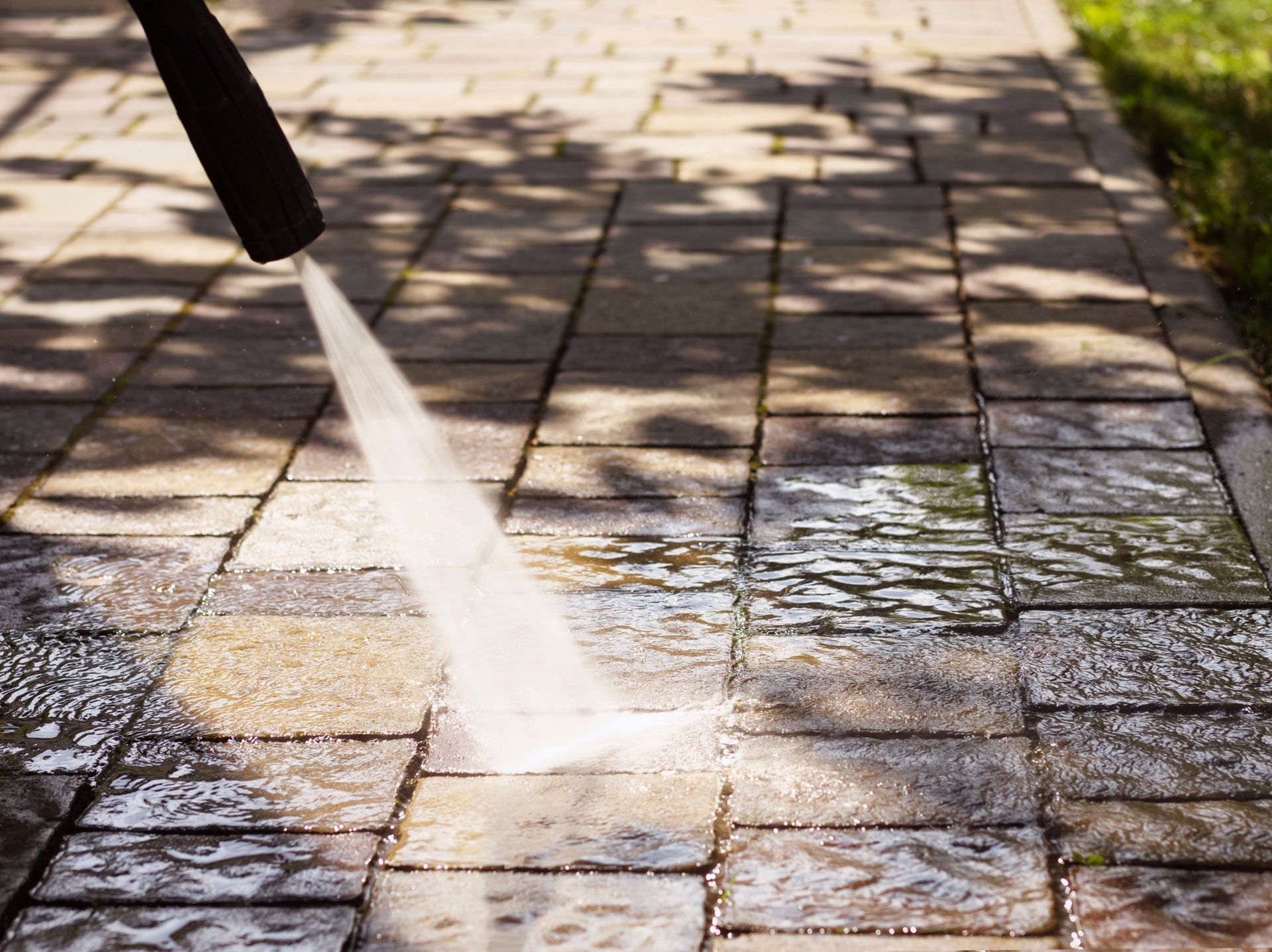Pressure washer spraying water on brick pavers.