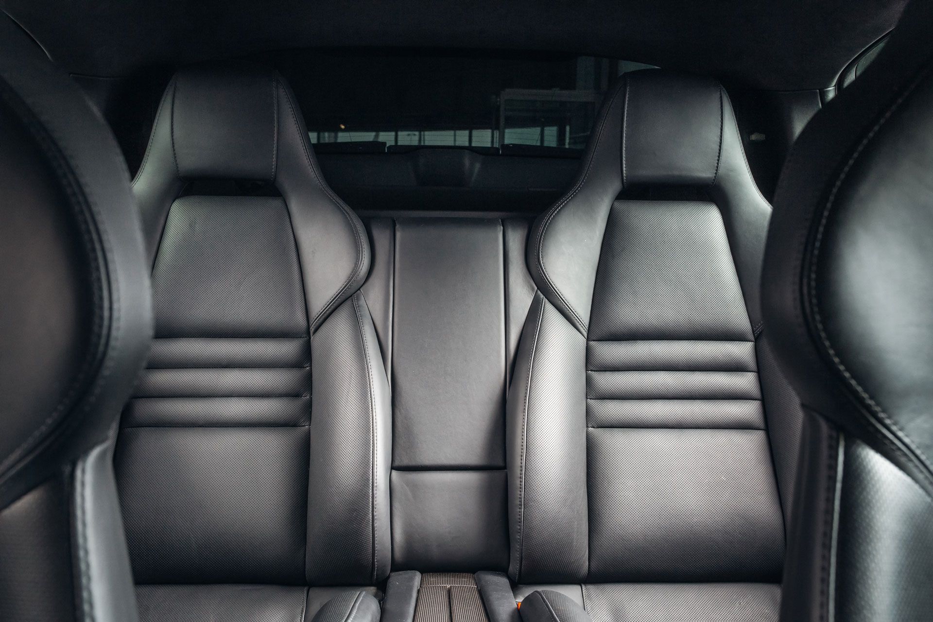 Black leather car seats in a rear passenger area, showing stitching details.