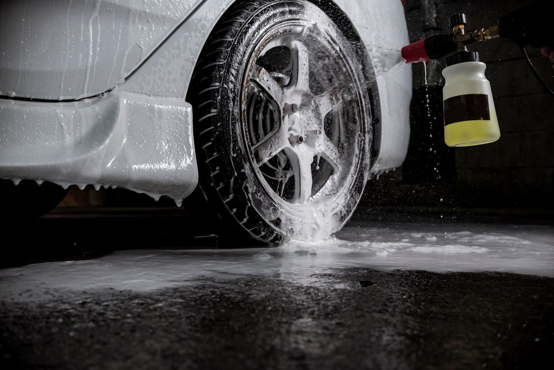 Car being washed, covered in white foam; wheel and body detail in focus.
