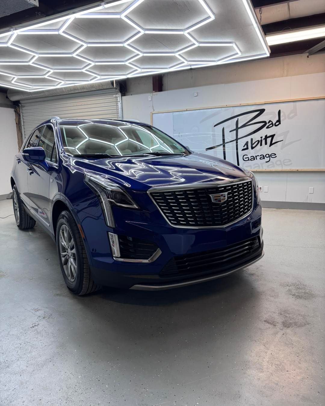 A dark blue Cadillac SUV parked in a garage with geometric ceiling lights and a 