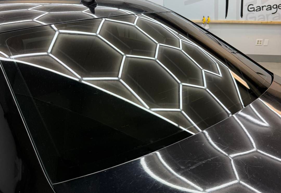 A high-angle view of a black car showing a reflection of hexagon-shaped ceiling lights on the windshield and roof.