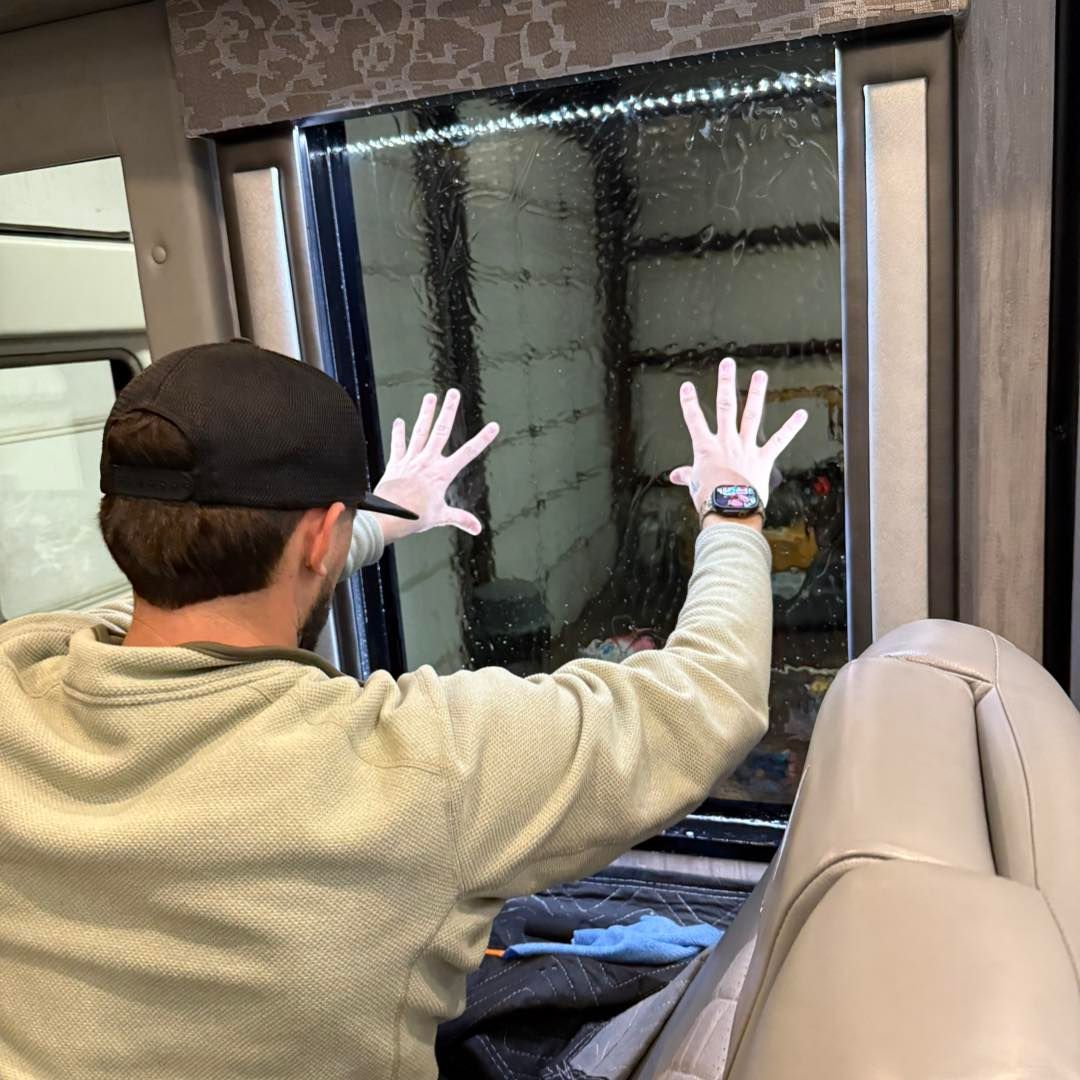 A person wearing a black cap and gloves presses their hands against a clean, tinted window inside a vehicle.