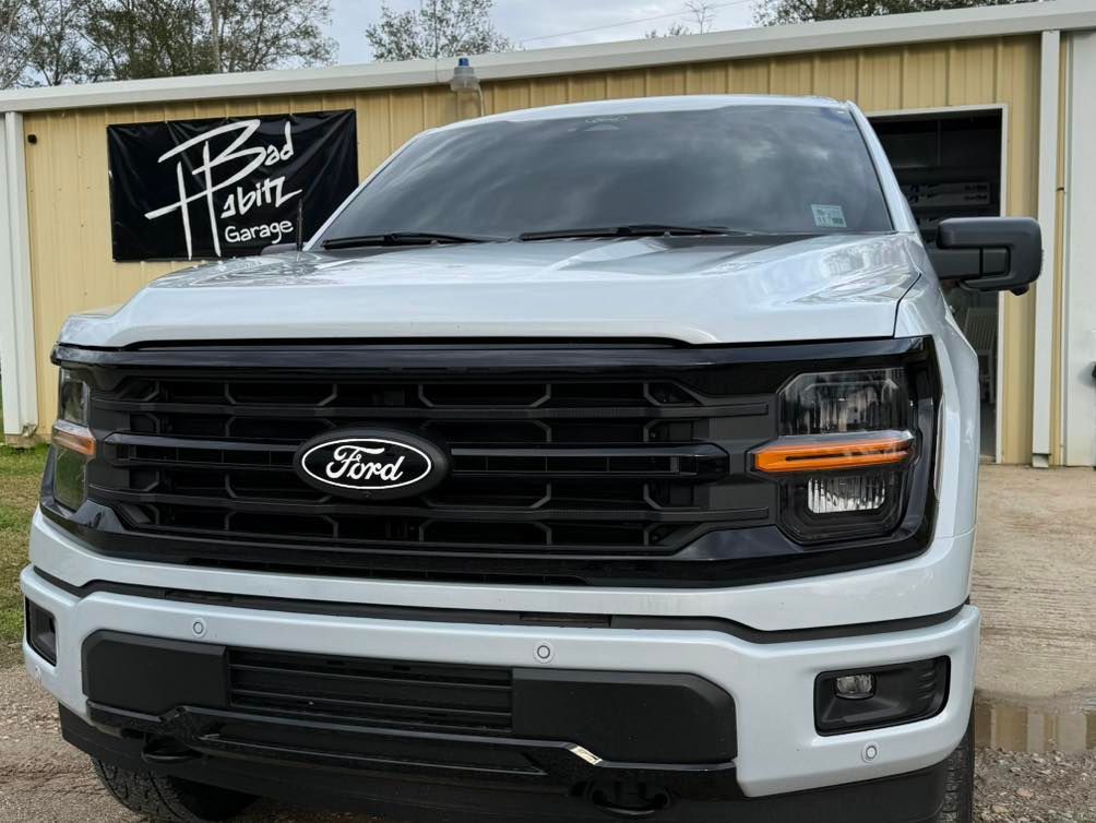 Front view of a white Ford F-150 truck with a black grille, parked in front of a 