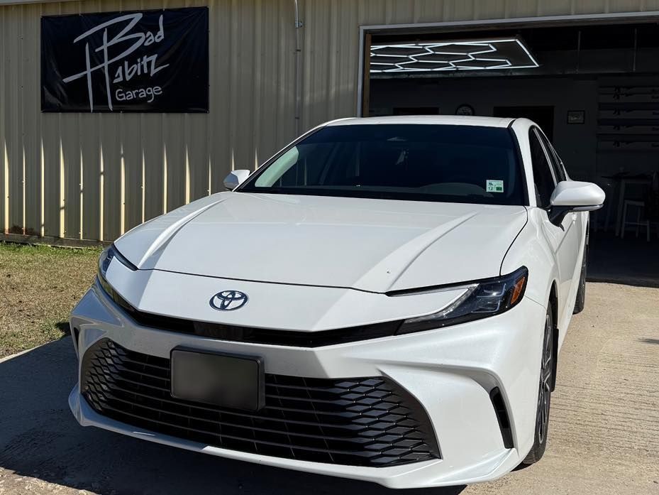 A white Toyota Camry parked outside a garage with a 