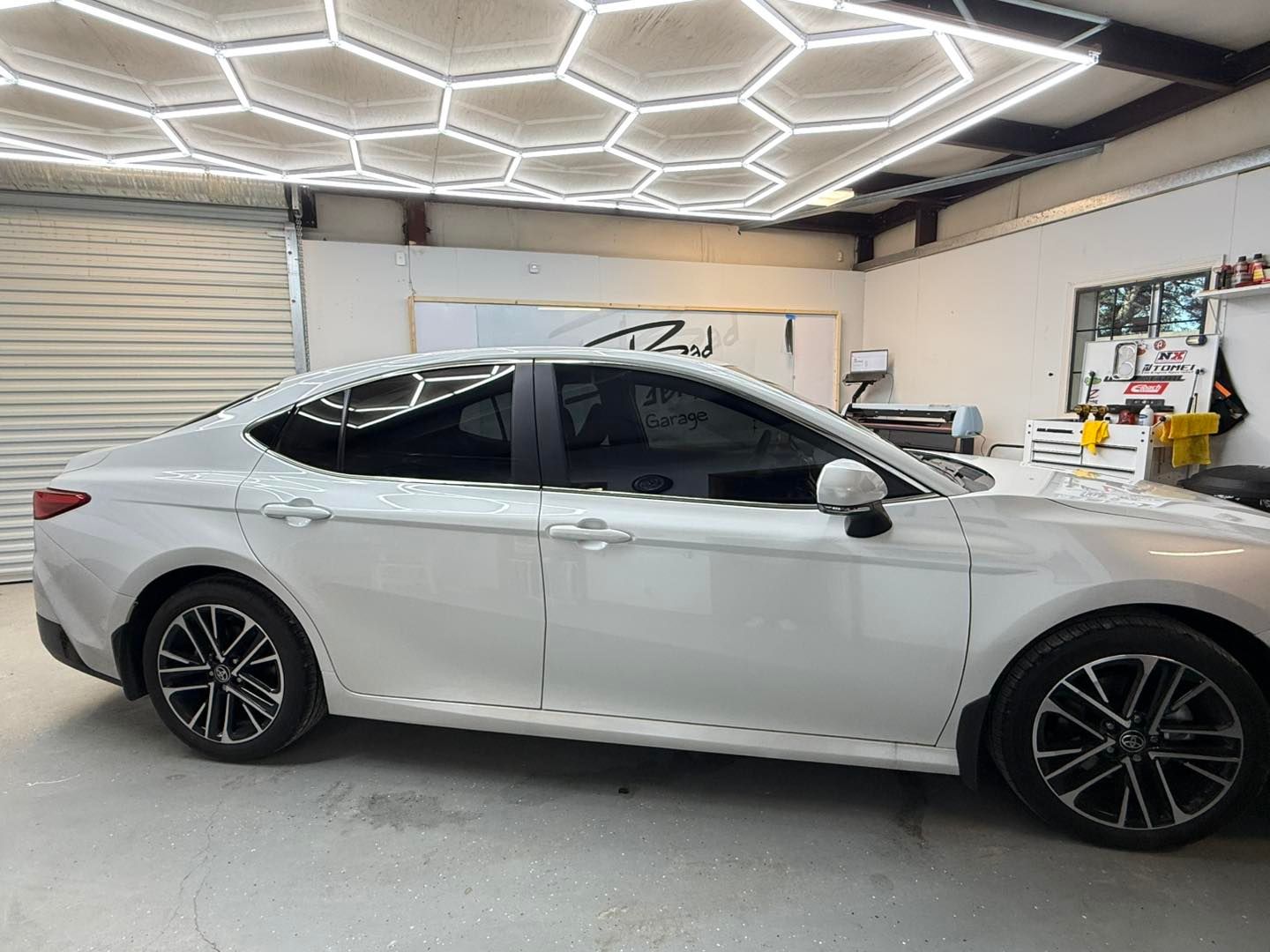 Side view of a white sedan parked inside a garage with geometric LED ceiling lights.