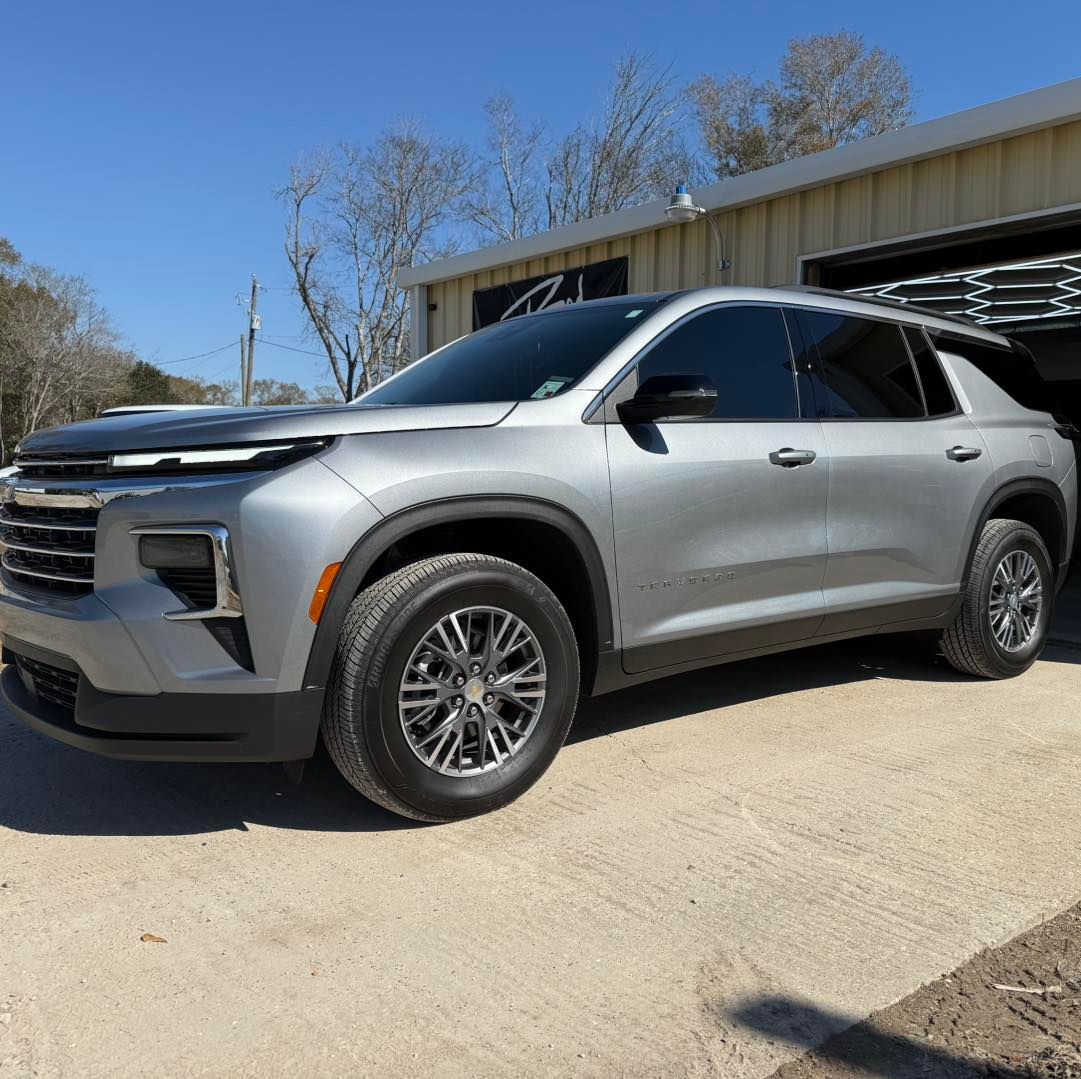 A silver Chevrolet Traverse parked on a concrete lot in front of a building under a clear blue sky.