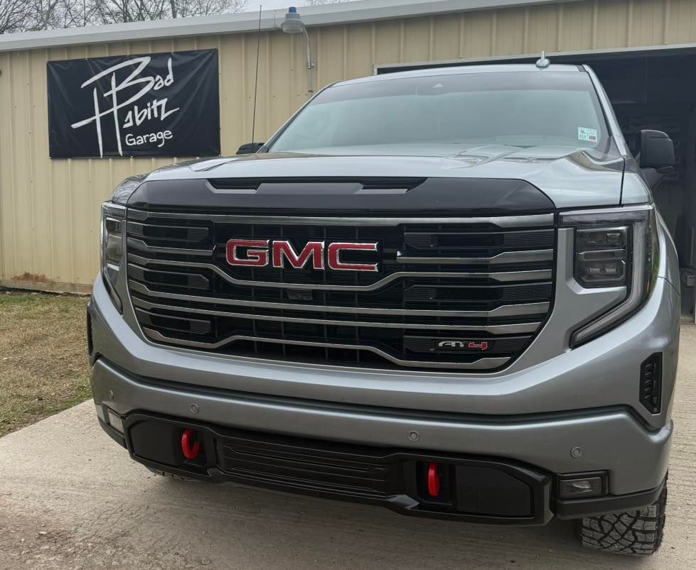 A silver GMC Sierra AT4 pickup truck parked in front of a building with a 