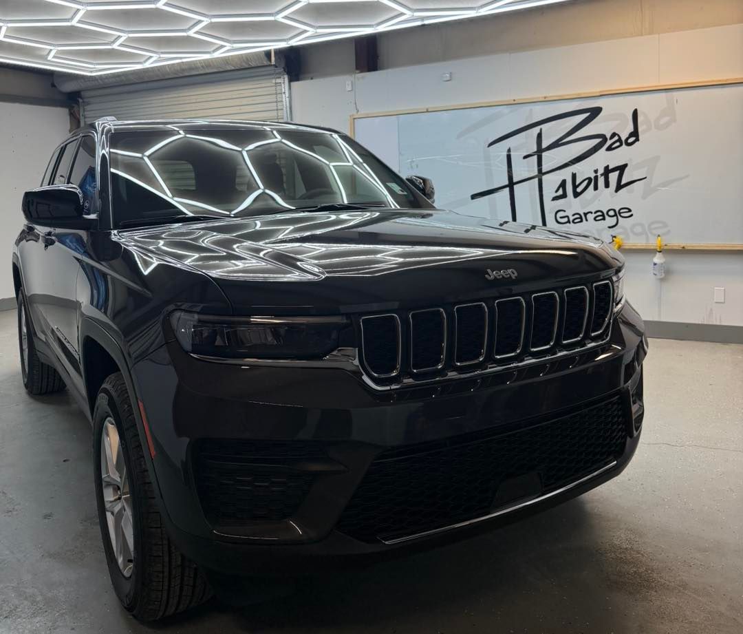 A black Jeep Grand Cherokee parked inside a garage with hexagonal ceiling lights and a 
