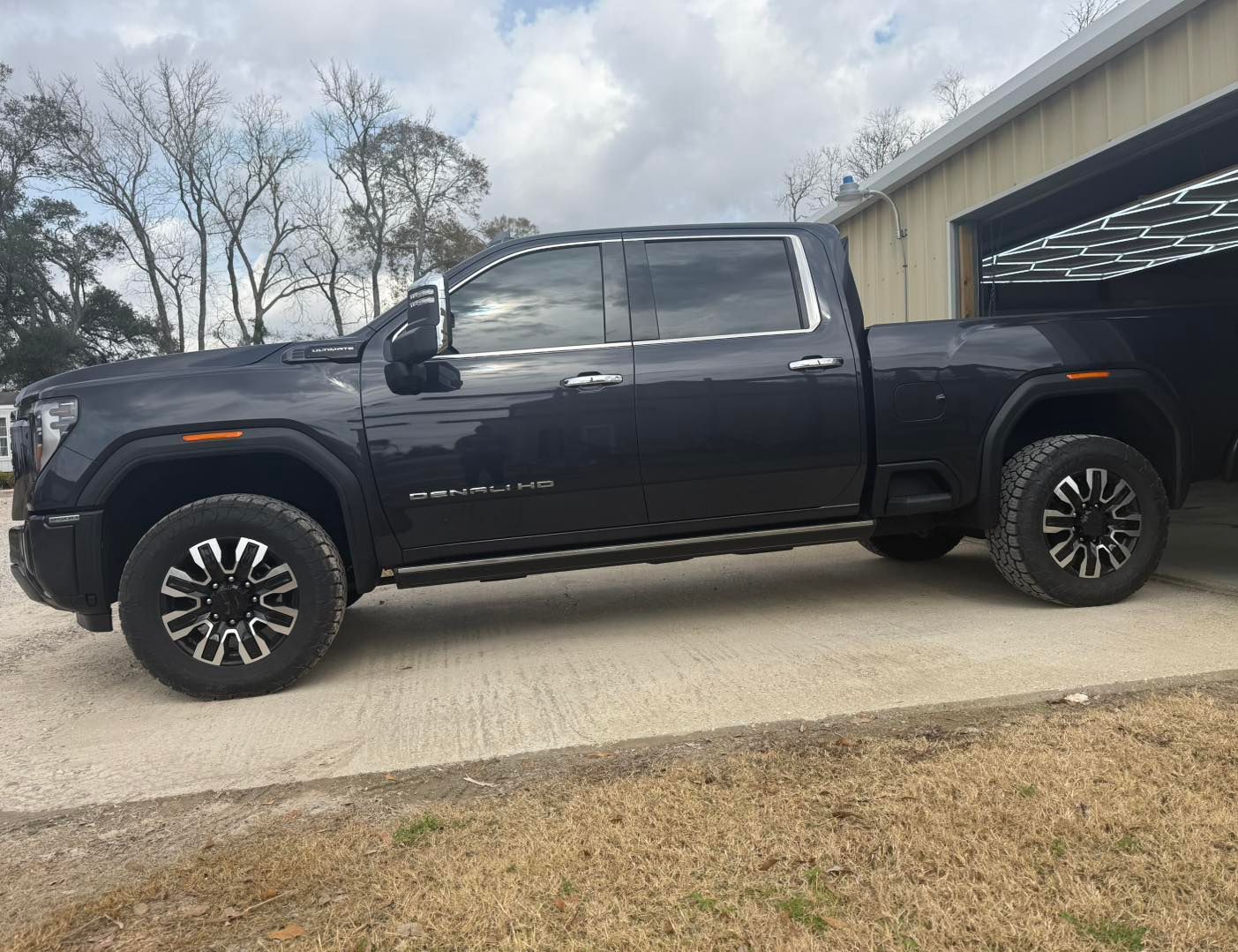 A dark gray GMC Sierra crew cab pickup truck parked on a concrete driveway in front of a building.