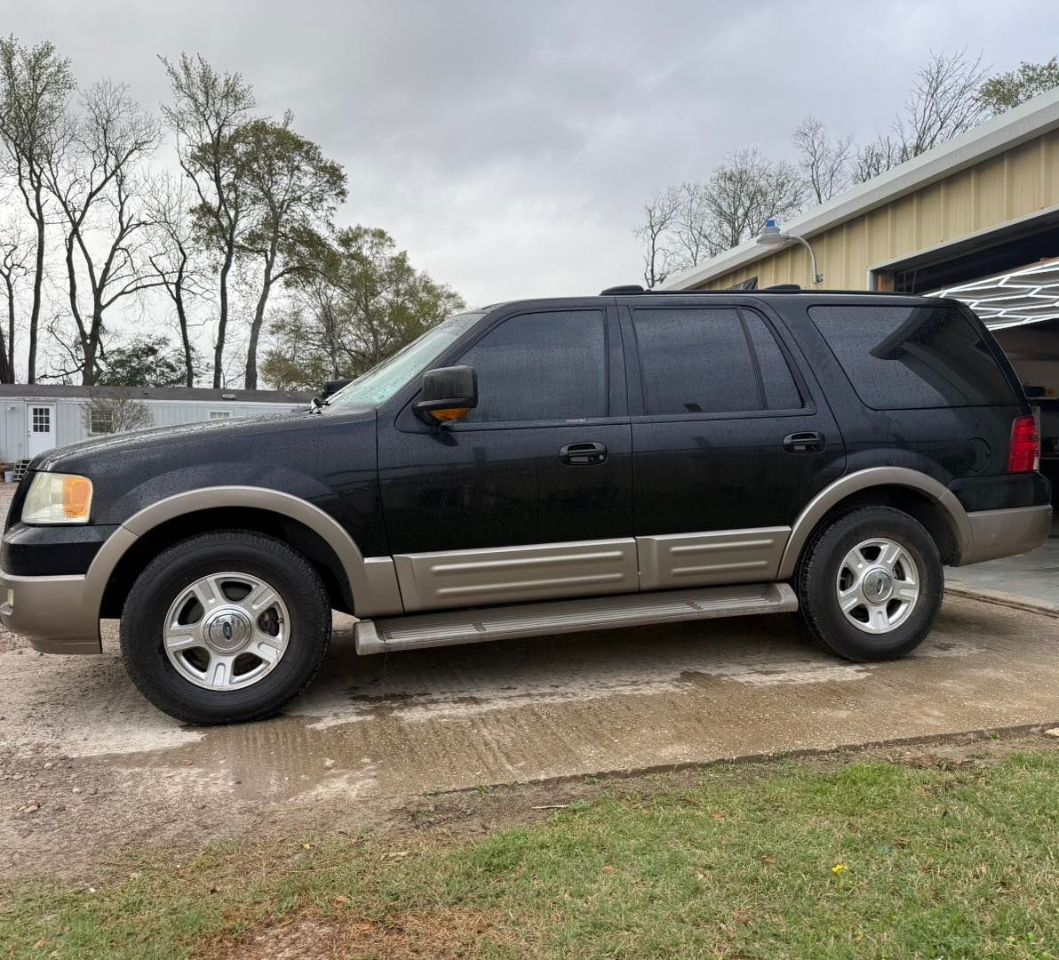A black and tan Ford Expedition SUV parked on a concrete driveway in front of a building.