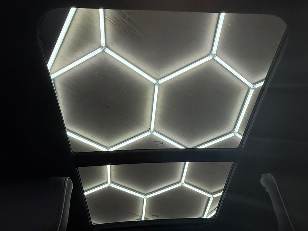 A ceiling-mounted light fixture featuring a bright white, honeycomb-patterned grid design against a dark background.